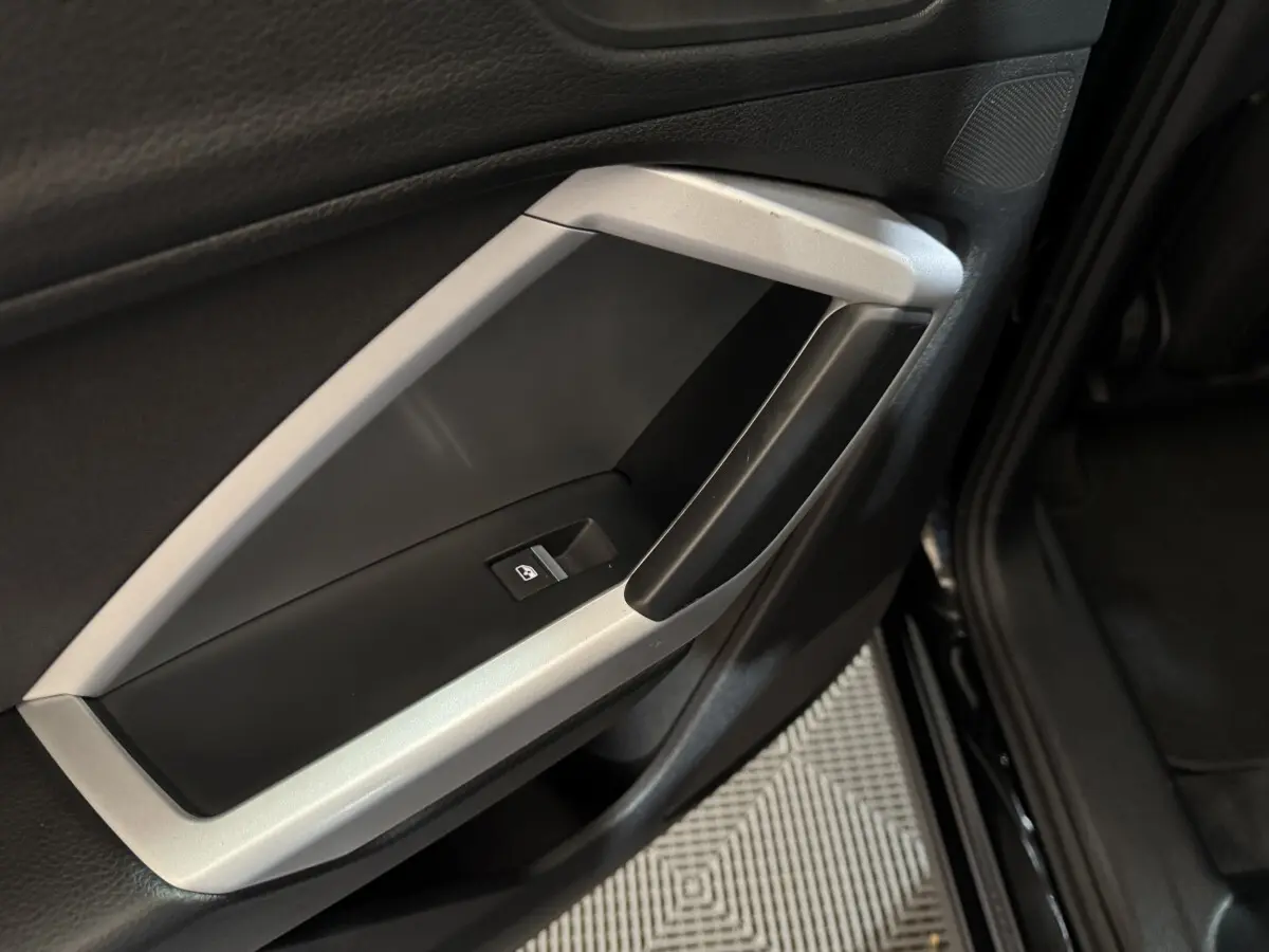 Poignée intérieure côté gauche de porte noire et argentée de l'Audi Q3 35 TFSI 2022 avec bouton de lève-vitre.