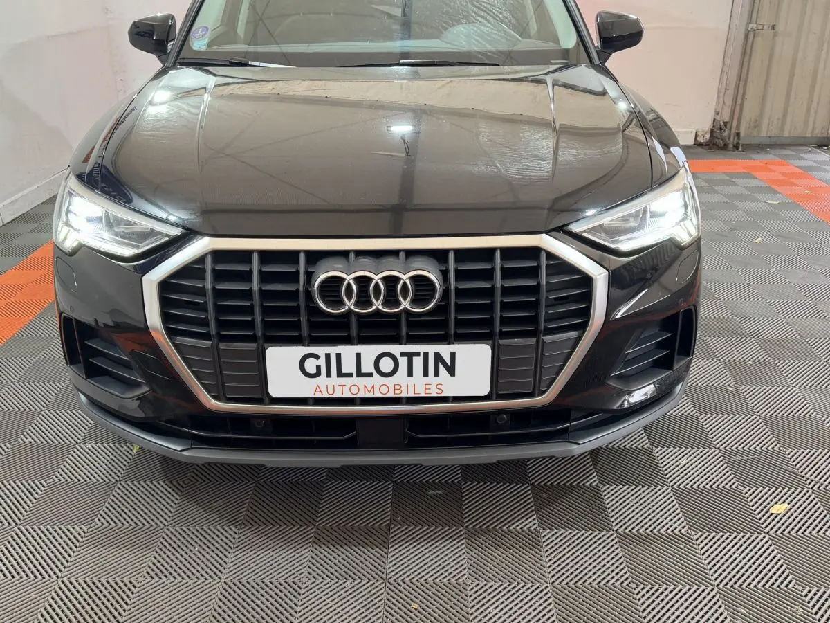 Vue frontale d'un Audi Q3 noir 2022 avec calandre hexagonale et phares LED allumés dans un garage.