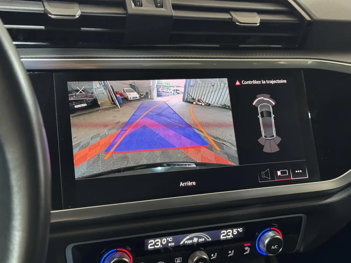 Écran tactile intérieur montrant la caméra de recul et l’aide au stationnement du tableau de bord d’un Audi Q3 noir.