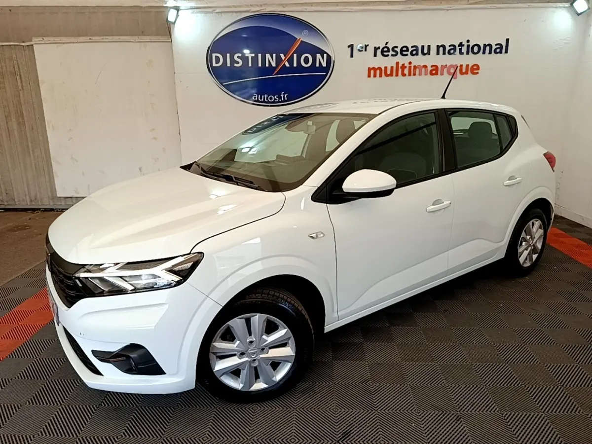 Vue 3/4 avant droit d'une Dacia Sandero Confort TCe 90 blanche, avec phares LED et jantes alliage en intérieur showroom.