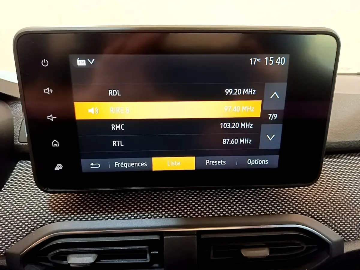 Écran tactile central affichant la radio FM dans l'habitacle d'une Dacia Sandero Confort blanc, vue de face rapprochée.