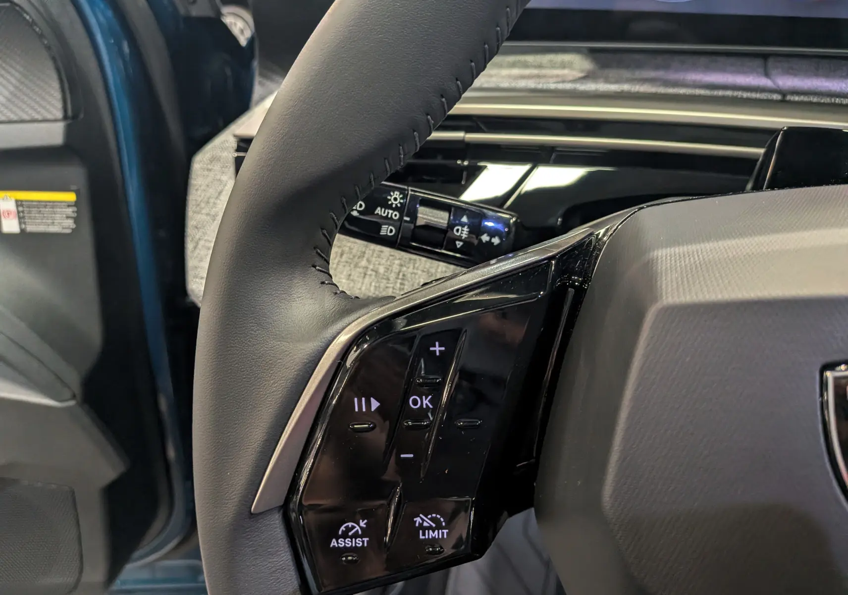 Gros plan sur la partie gauche du volant noir du Peugeot 3008 Hybrid 2026 Bleu Obsession, avec commandes intégrées.
