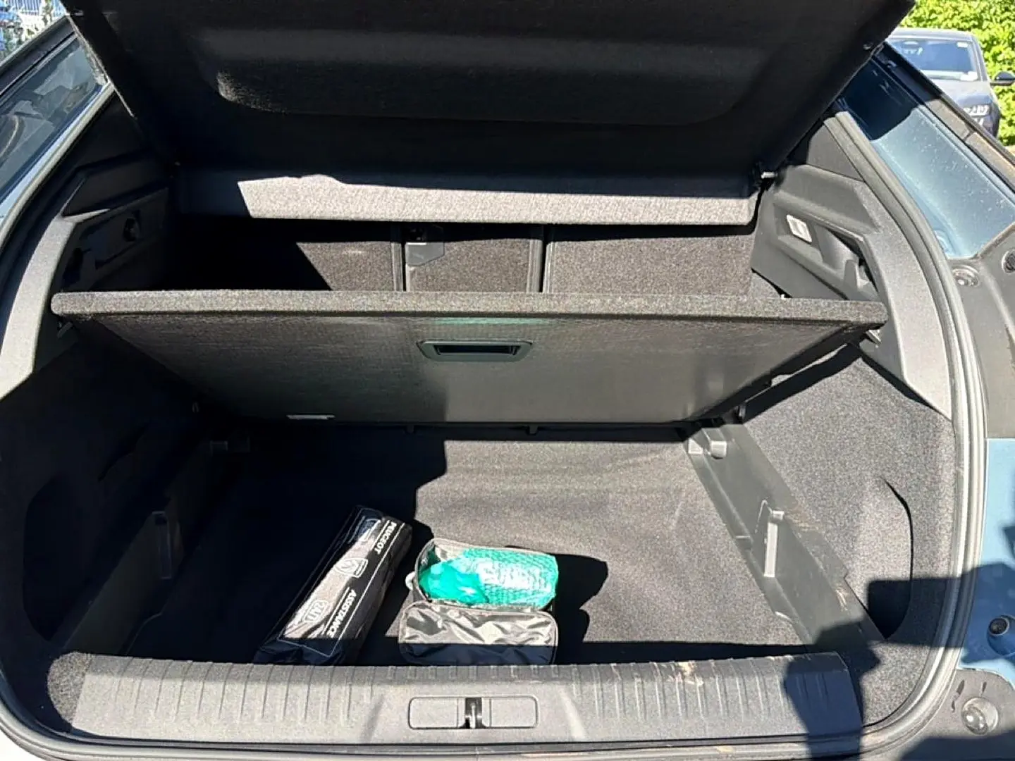 Coffre ouvert vu de l'arrière d'un Peugeot 3008 bleu Ingara, avec plancher mobile et accessoires rangés.