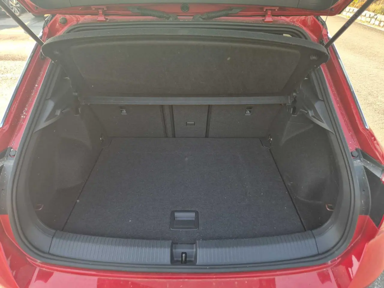 Coffre ouvert vu de l'arrière d'un Volkswagen T-Roc rouge métal foncé, espace de chargement vide et propre.