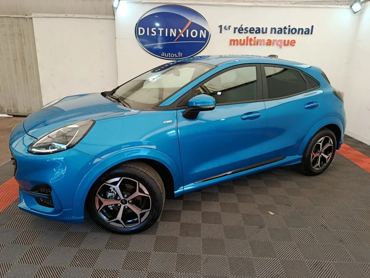 Vue latérale droite d'un Ford Puma bleu 2025 ST-LINE avec jantes alliage et vitres teintées en intérieur showroom.