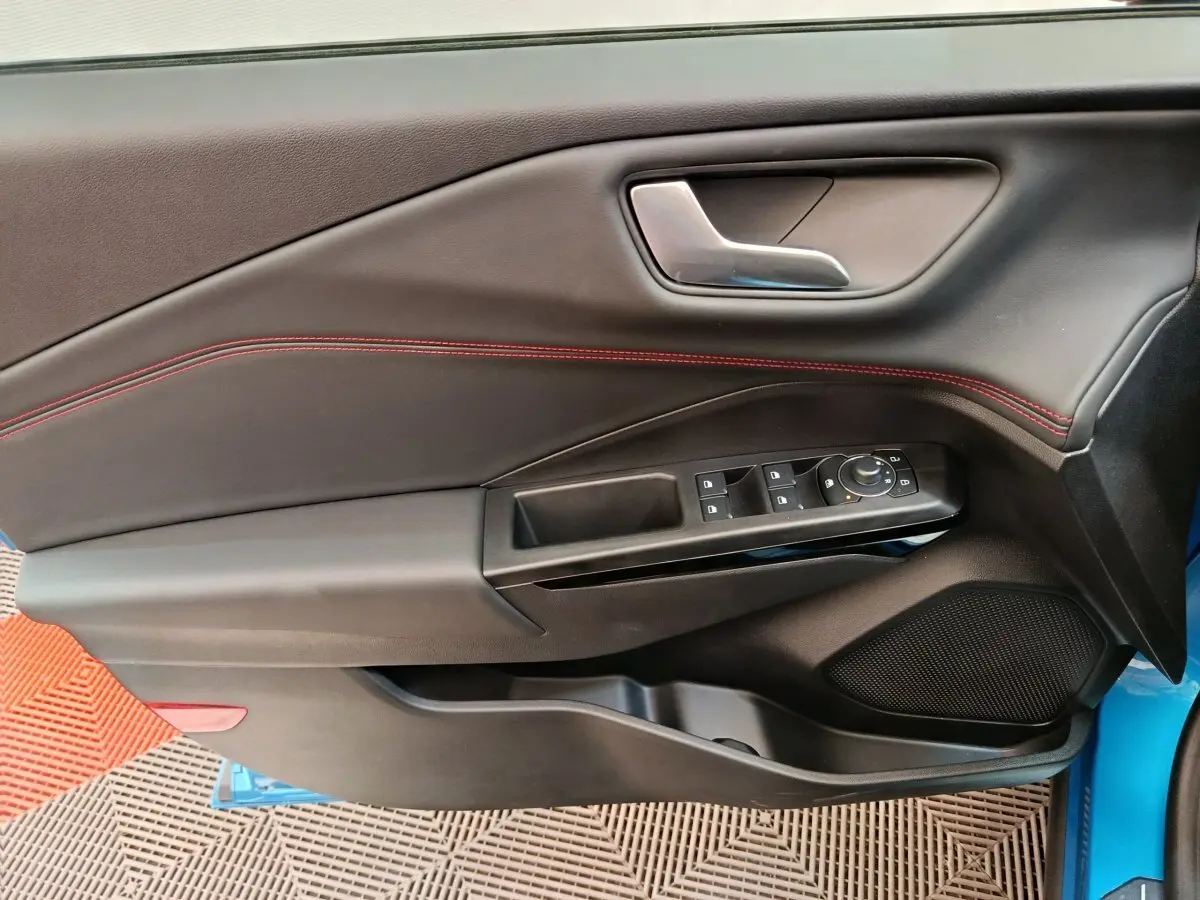 Gros plan sur la porte avant gauche du Ford Puma bleu, avec commandes électriques et surpiqûres rouges visibles.