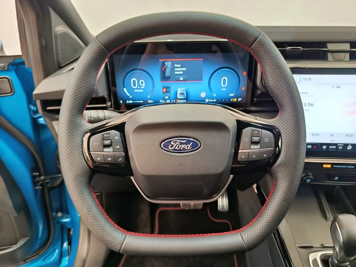 Vue frontale du volant en cuir noir avec surpiqûres rouges du Ford Puma bleu, tableau de bord numérique et écran tactile visibles.
