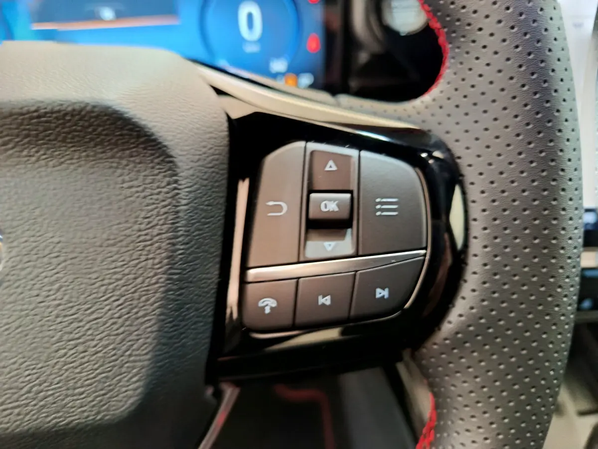 Gros plan sur les commandes multifonctions à droite du volant en cuir perforé avec surpiqûres rouges du Ford Puma 2025.