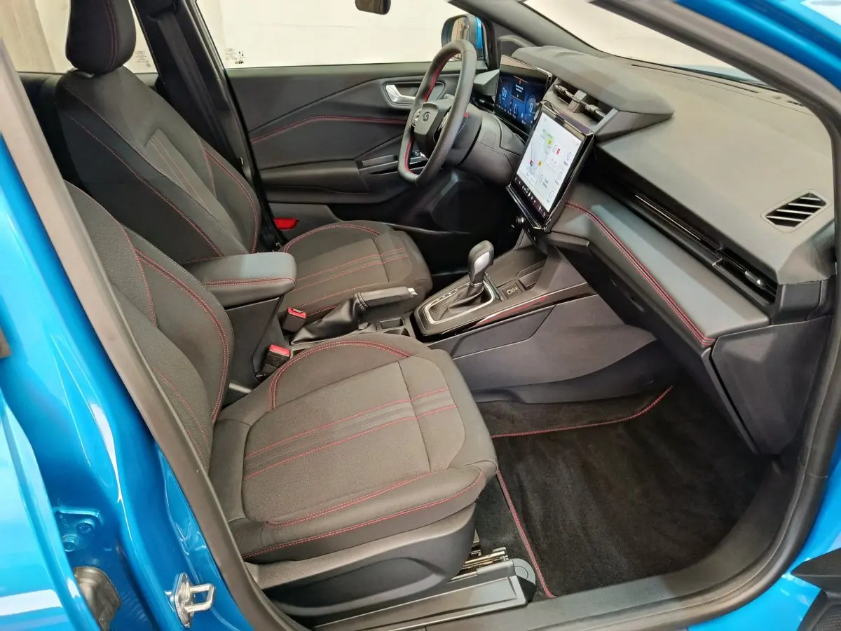 Intérieur avant droit du Ford Puma bleu 2025, sièges noirs avec surpiqûres rouges et tableau de bord digital tactile.
