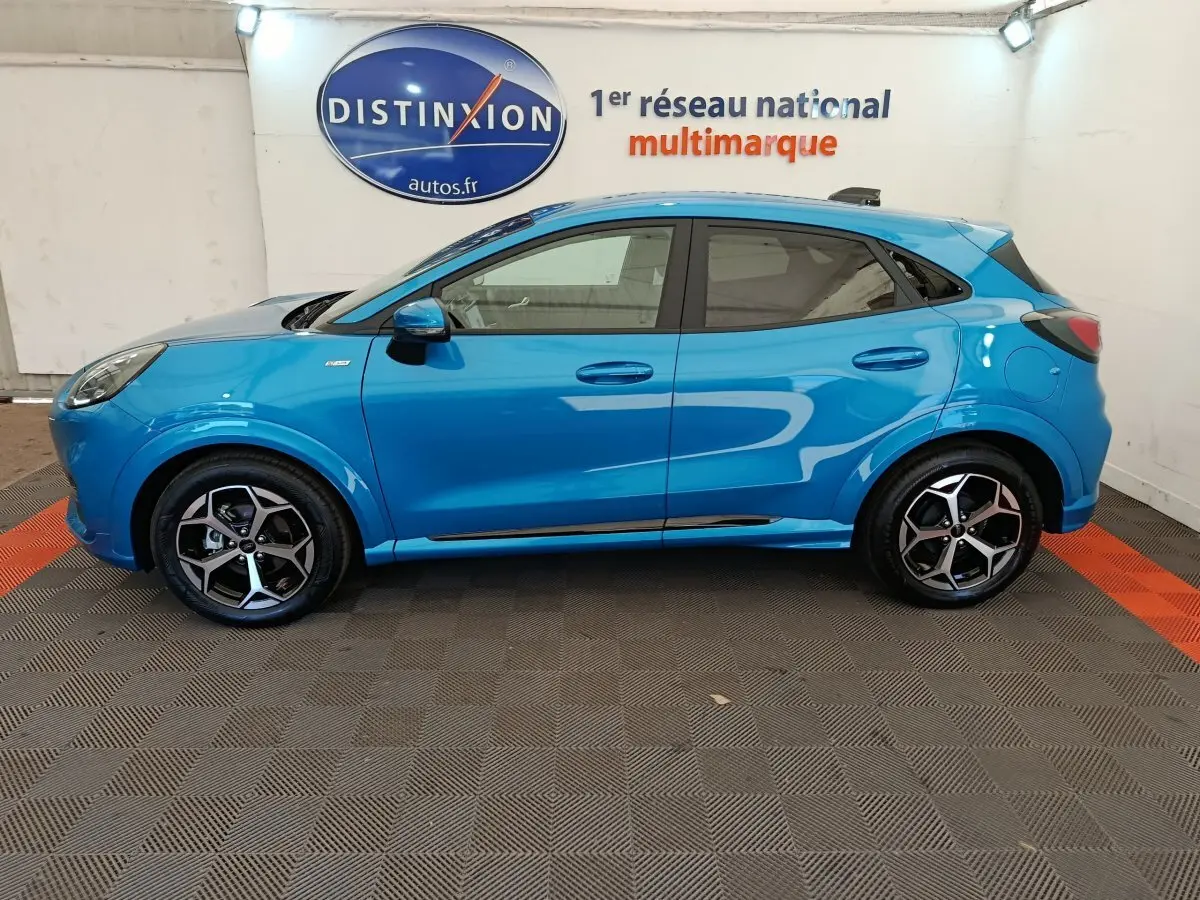 Profil côté gauche d'un Ford Puma bleu 2025 ST-LINE avec jantes alliage et logo Distinxion en arrière-plan.