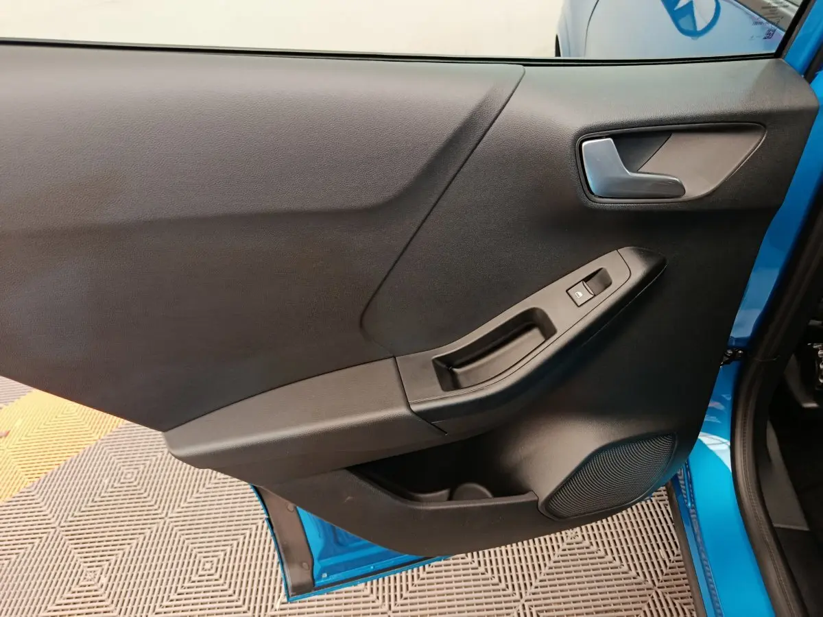 Vue rapprochée de la porte avant gauche noire du Ford Puma bleu 2025, avec poignée et commande de fenêtre électrique.