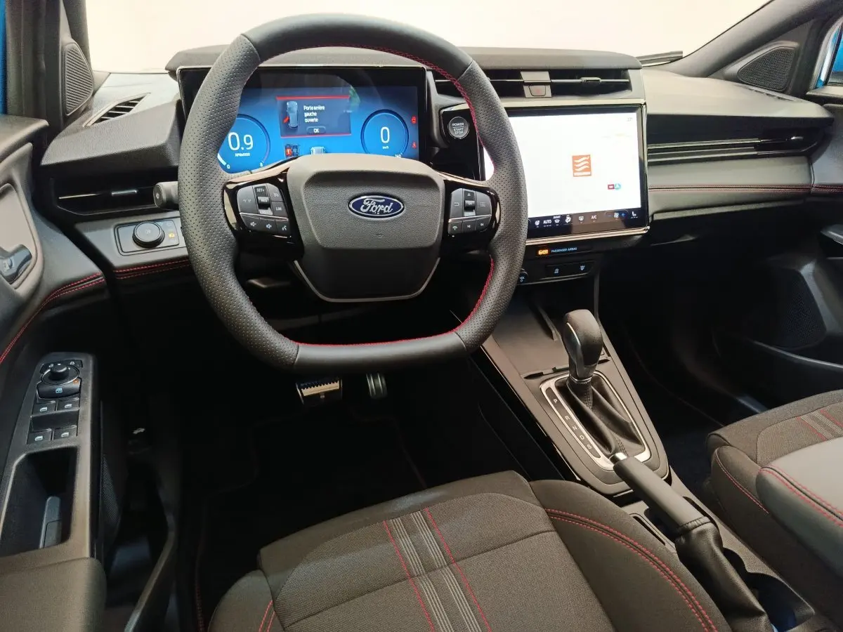 Vue intérieure avant du Ford Puma bleu 2025, volant cuir noir avec surpiqûres rouges et écran tactile central lumineux.