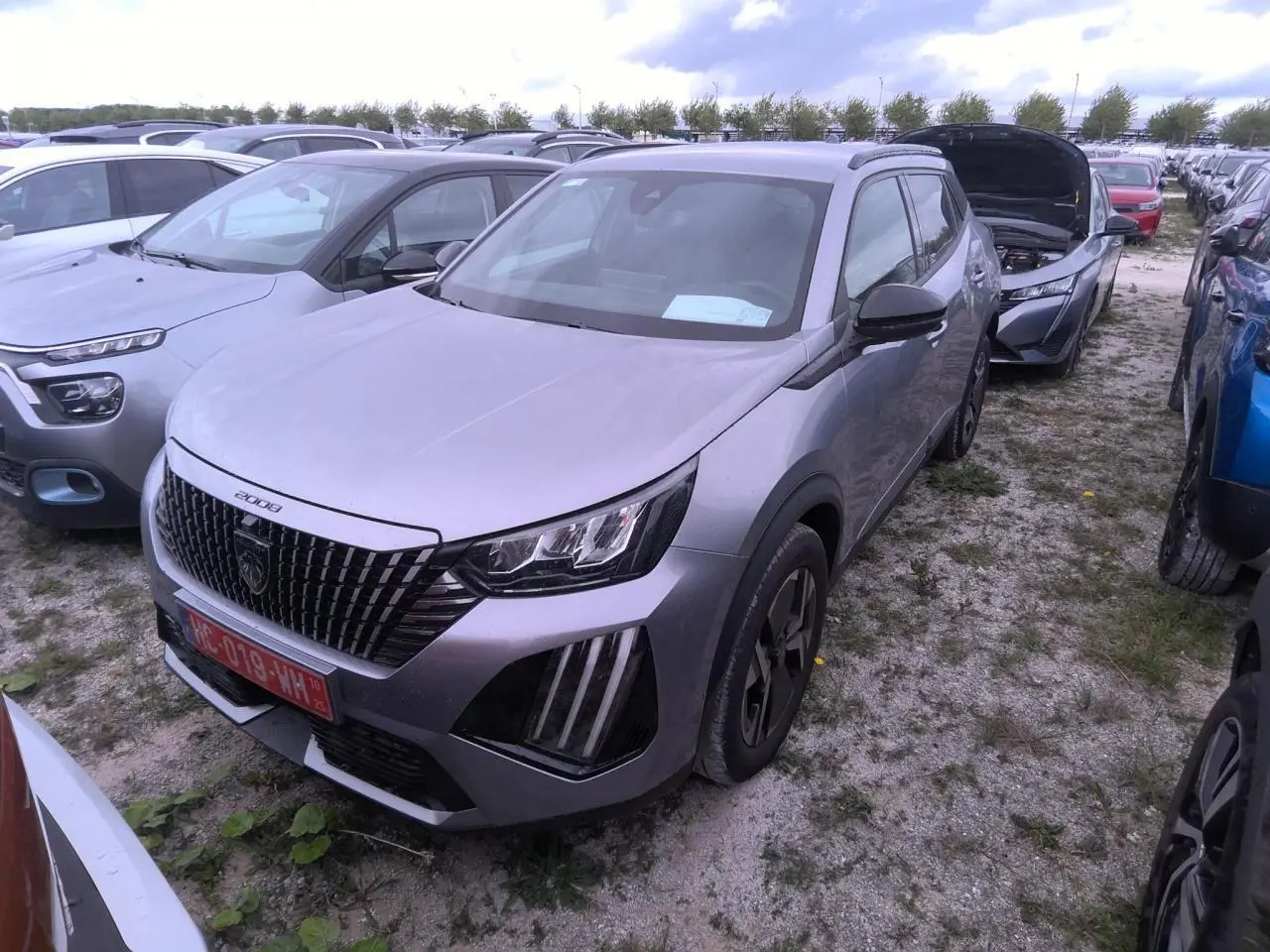 Peugeot 2008 gris clair vue 3/4 avant droit, calandre noire avec marquage vertical et feux LED griffés.