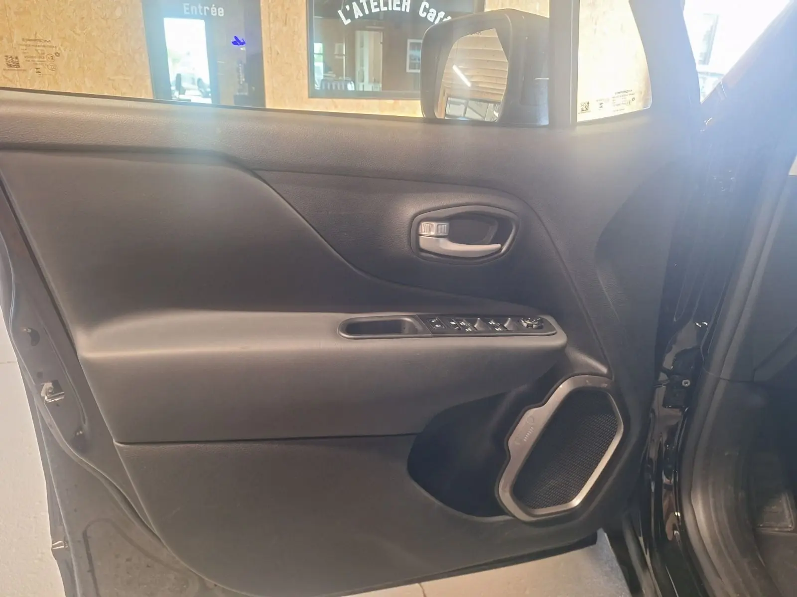 Vue intérieure de la porte côté gauche noire du Jeep Renegade 2024 avec haut-parleur et commandes électriques visibles.