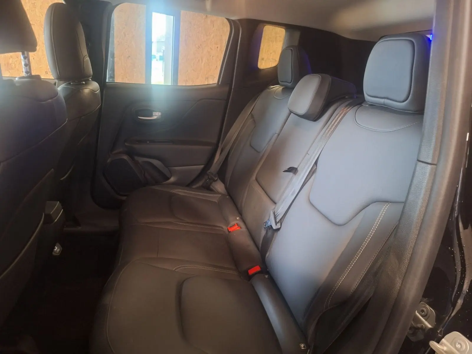 Vue intérieure côté droit des sièges arrière en cuir noir du Jeep Renegade 2024 hybride, avec ceintures de sécurité visibles.