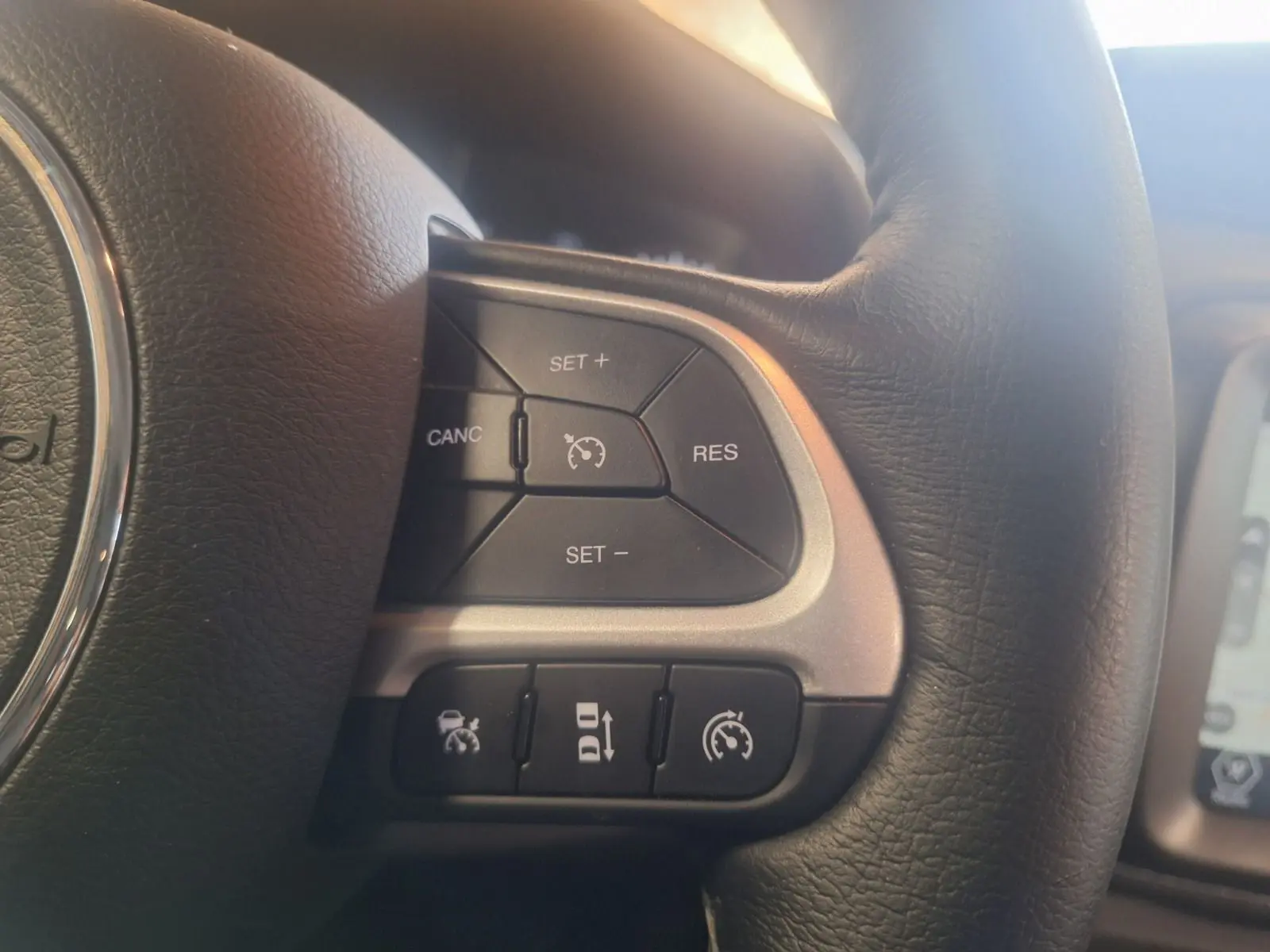 Gros plan sur les commandes de régulateur de vitesse au volant cuir noir du Jeep Renegade 2024 hybride.