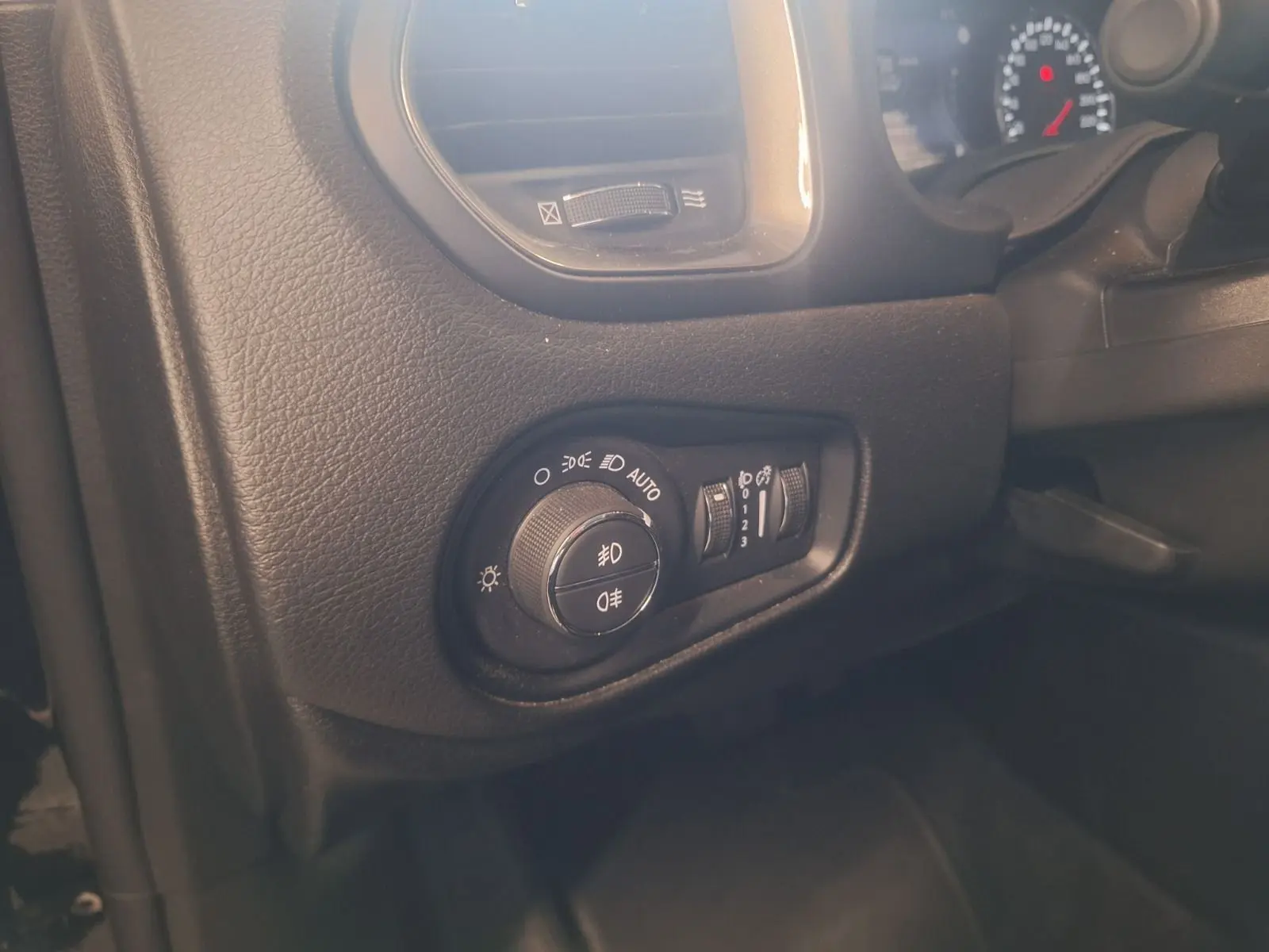 Gros plan sur les commandes d'éclairage à gauche du tableau de bord du Jeep Renegade noir 2024.