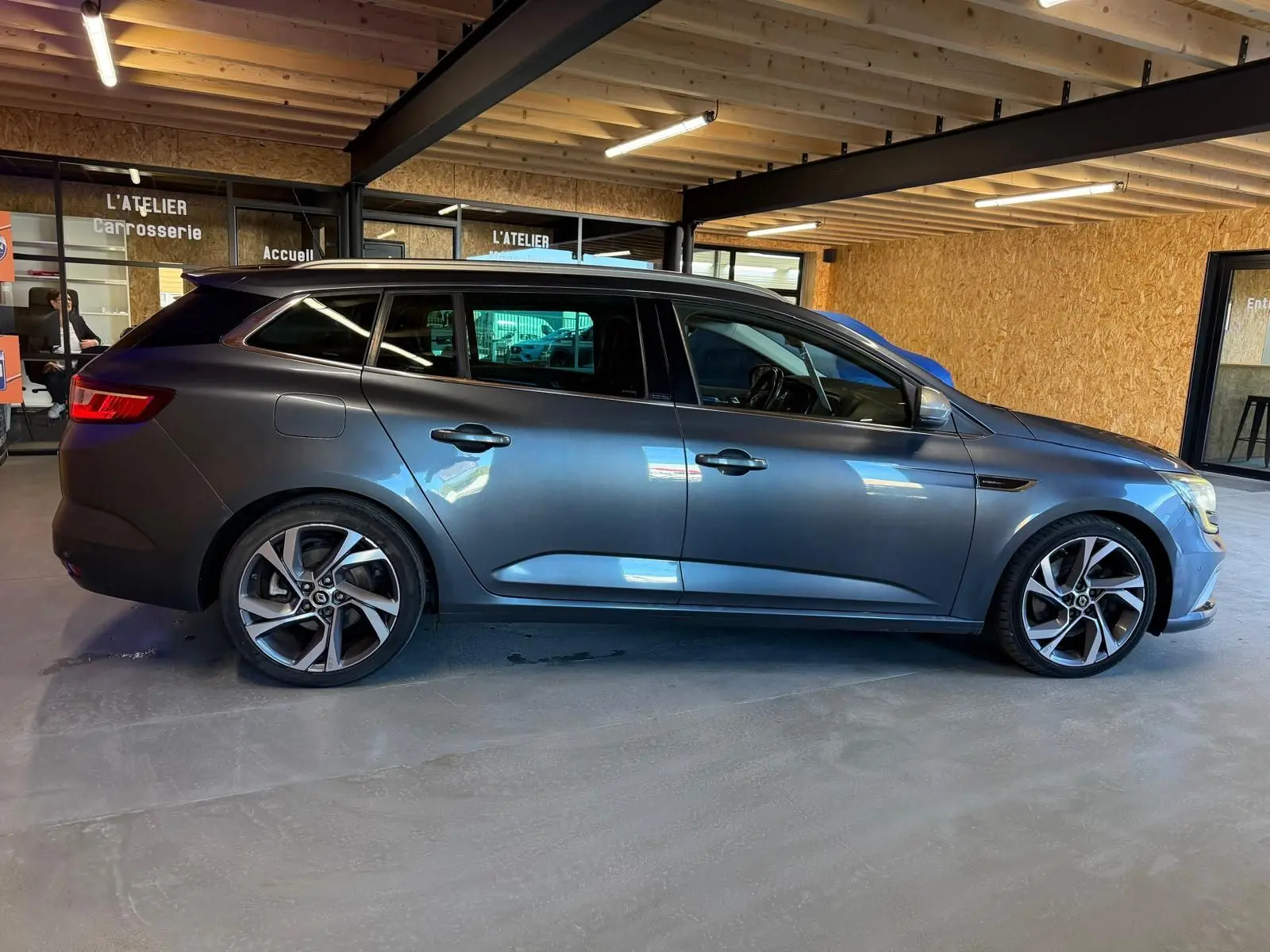Profil droit d’une Renault Mégane Break GT gris métallisé, stationnée en intérieur avec jantes alliage distinctives.