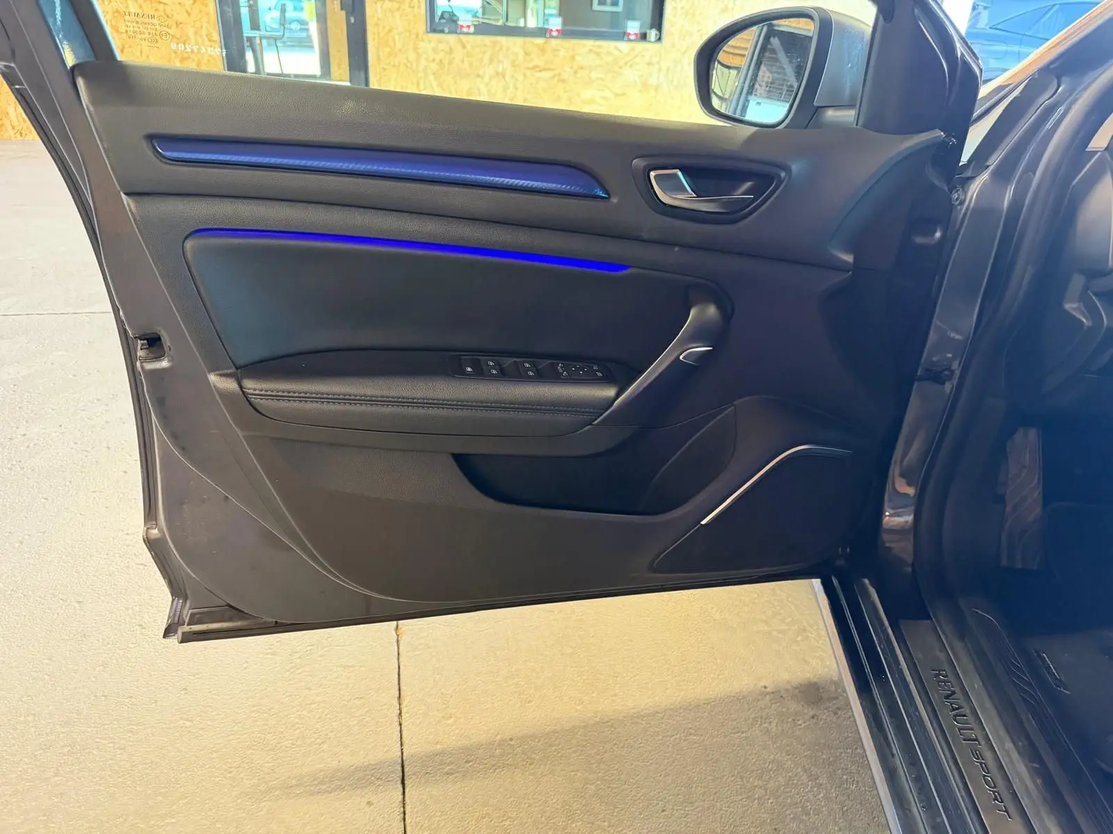 Vue rapprochée de la porte avant gauche ouverte d’une Renault Mégane Break GT grise, avec éclairage d’ambiance bleu sur la garniture.