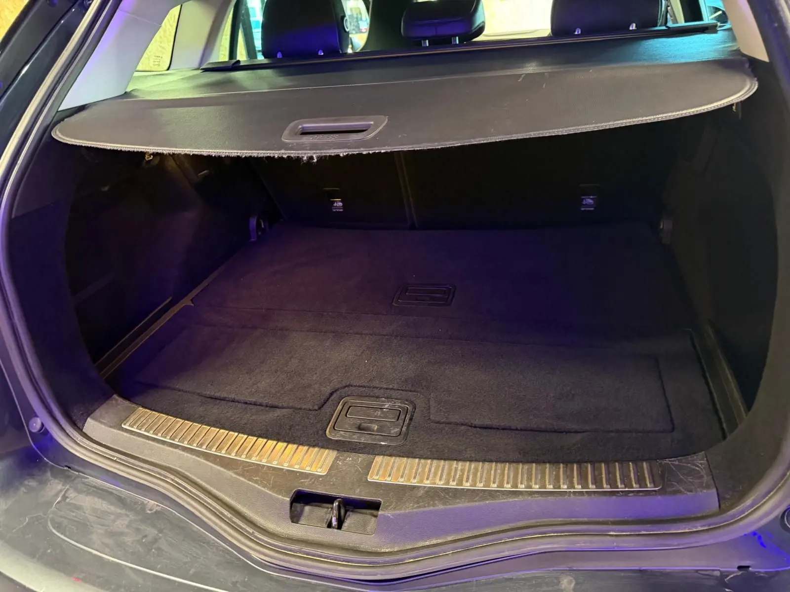 Coffre ouvert vu de l'arrière d'une Renault Mégane Break gris, avec cache-bagages et tapis noir.