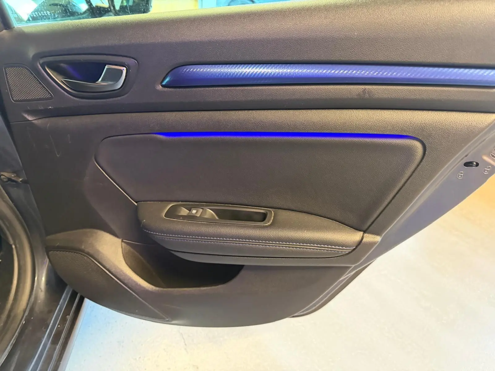 Vue intérieure côté gauche de la porte arrière d’une Renault Mégane Break gris avec éclairage d’ambiance bleu.