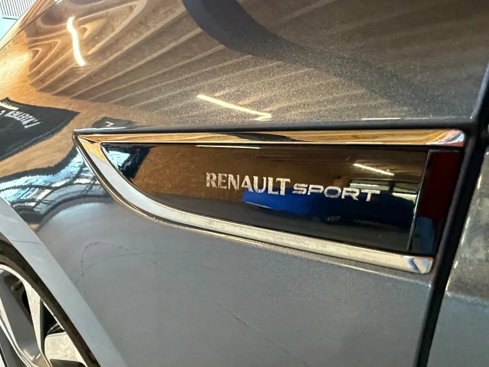 Gros plan sur l’inscription Renault Sport sur la carrosserie grise d’un Renault Mégane Break GT, côté avant droit.