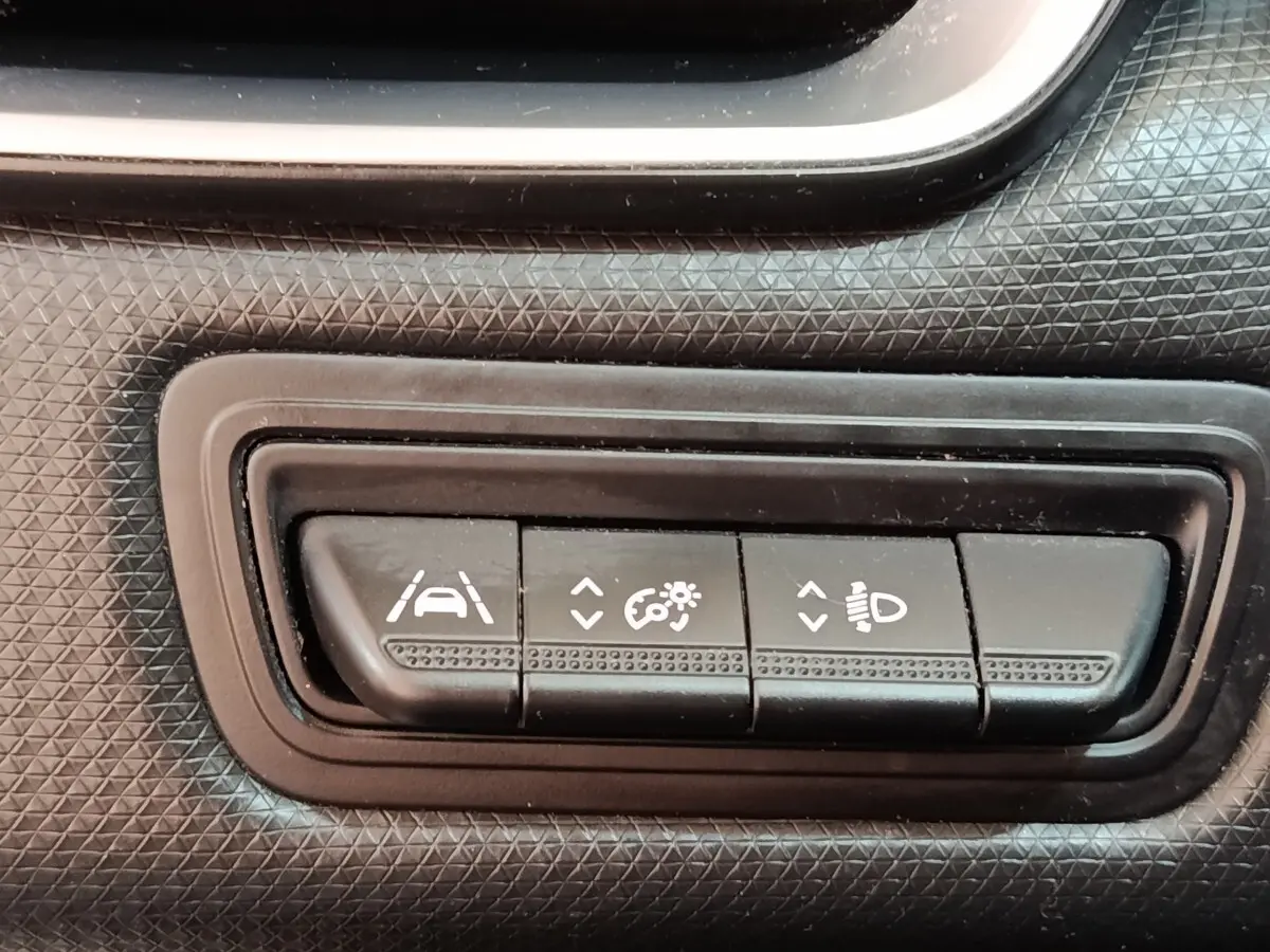 Gros plan sur les boutons de réglage d'assistance et phares du tableau de bord noir de la Renault Clio Business Blue dCi 100 blanche.