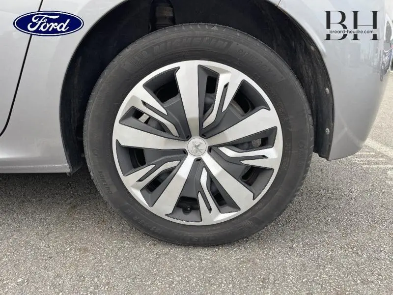 Gros plan sur la roue avant gauche d'une Peugeot 208 gris Artense avec jante en alliage au design moderne.