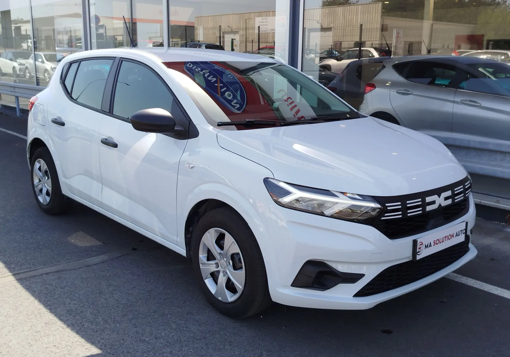 Vue 3/4 avant droite d'une Dacia Sandero blanche Glacier 2025 avec calandre noire et feux LED distinctifs.