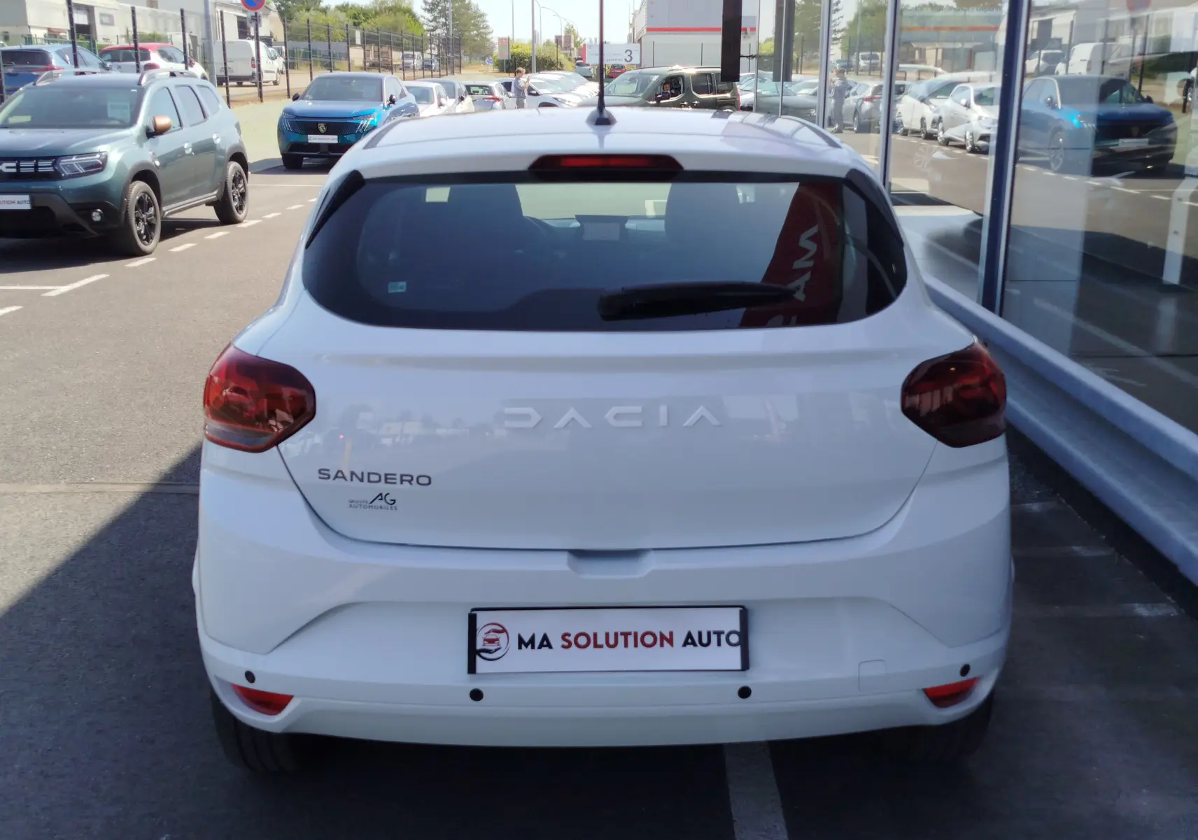 Vue arrière d'une Dacia Sandero blanc glacier 2025, avec feux arrière rouges et logo visible sur un parking extérieur.