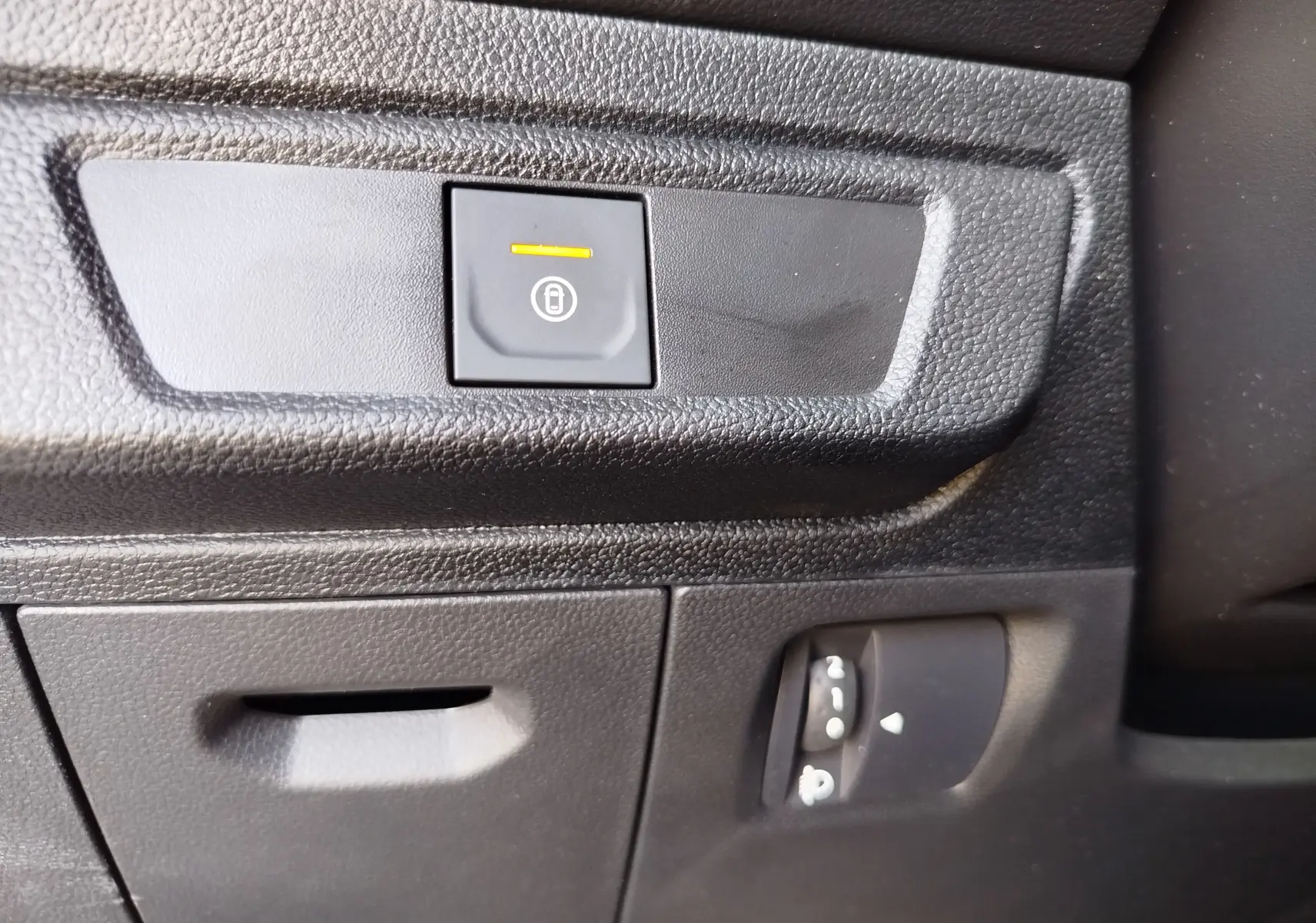 Gros plan sur le bouton de verrouillage centralisé avec témoin orange dans l'habitacle noir du Dacia Sandero 2025.