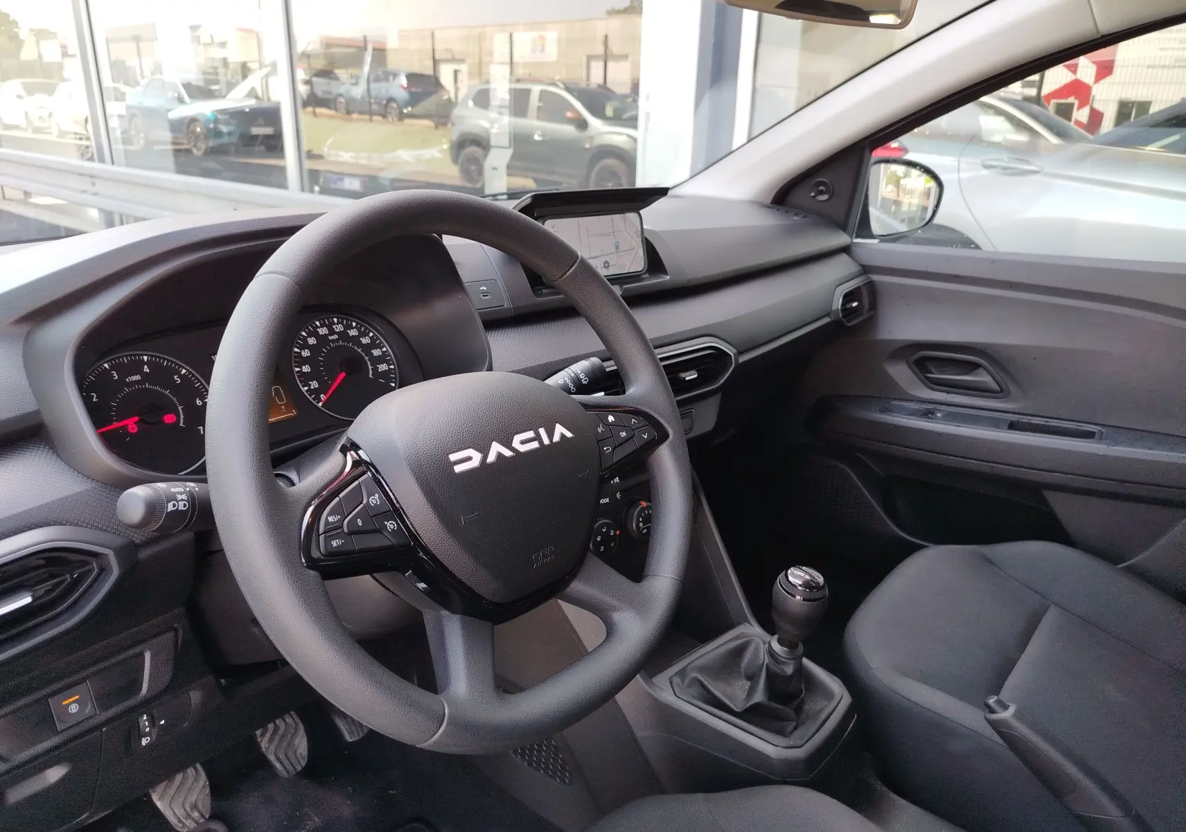 Vue intérieure côté conducteur de la Dacia Sandero 2025, volant multifonction et levier de vitesse manuel visibles.