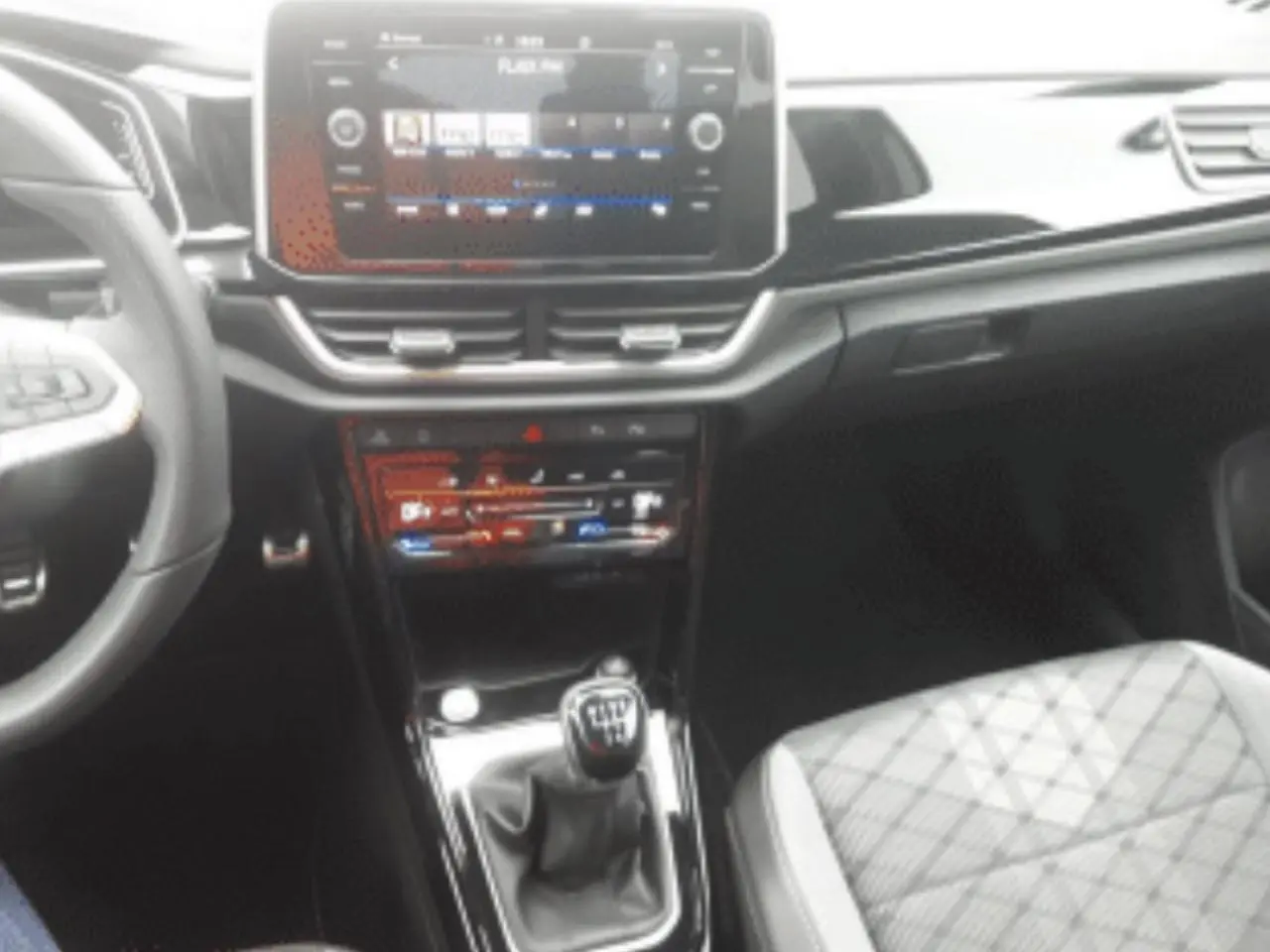 Vue intérieure centrée sur la console centrale et levier de vitesse manuel du Volkswagen T-Roc gris platinium 2025.