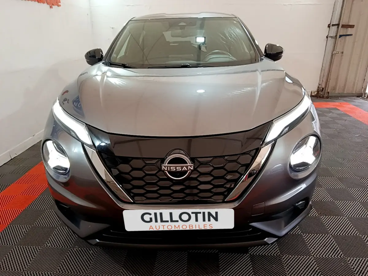 Vue frontale d'un Nissan Juke Hybrid 143 Business+ gris foncé avec phares LED allumés et calandre noire hexagonale.