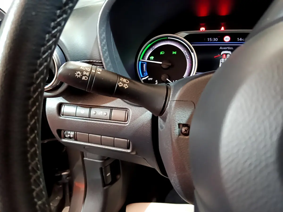 Gros plan sur le combiné d'instruments et la commande des phares à gauche du volant du Nissan Juke Hybrid 2023 gris foncé.