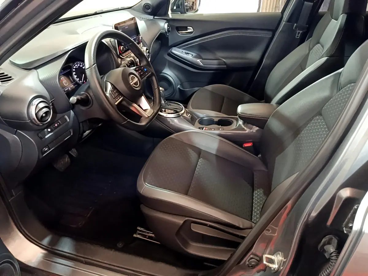 Intérieur du Nissan Juke Hybrid 143 Business+ 2023 vu côté conducteur, sièges noirs et tableau de bord moderne.