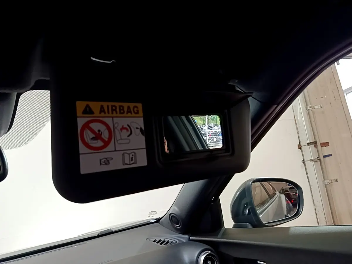 Détail du pare-soleil côté conducteur avec miroir et avertissement airbag dans le Nissan Juke Hybrid gris foncé 2023