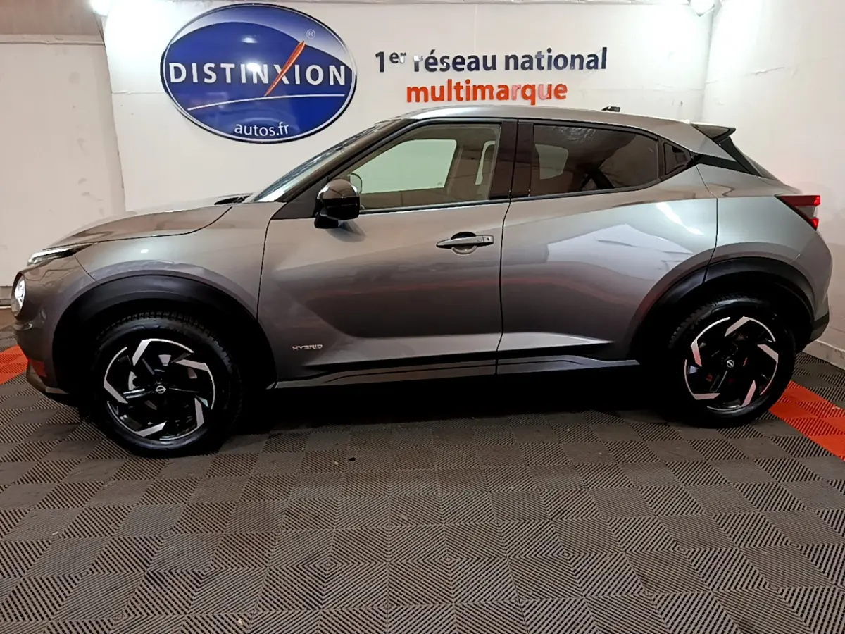 Profil côté gauche du Nissan Juke Hybrid 143 Business+ gris foncé, avec jantes noires et détails hybrides visibles.