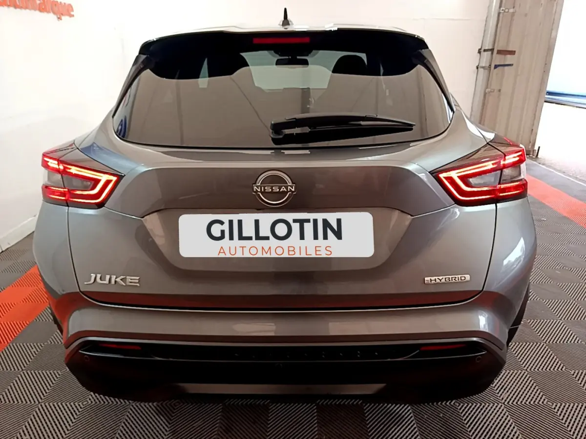 Vue arrière du Nissan Juke Hybrid gris foncé 2023 avec feux LED allumés et logo visible sur un sol damier noir et rouge.