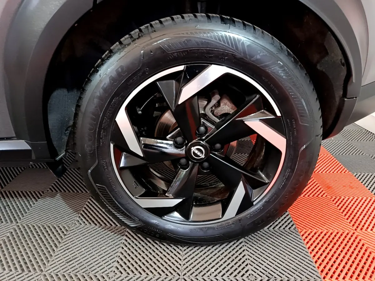 Gros plan sur la jante noire et argentée d'un Nissan Juke Hybrid 143 Business+ gris foncé, avec pneu Goodyear.