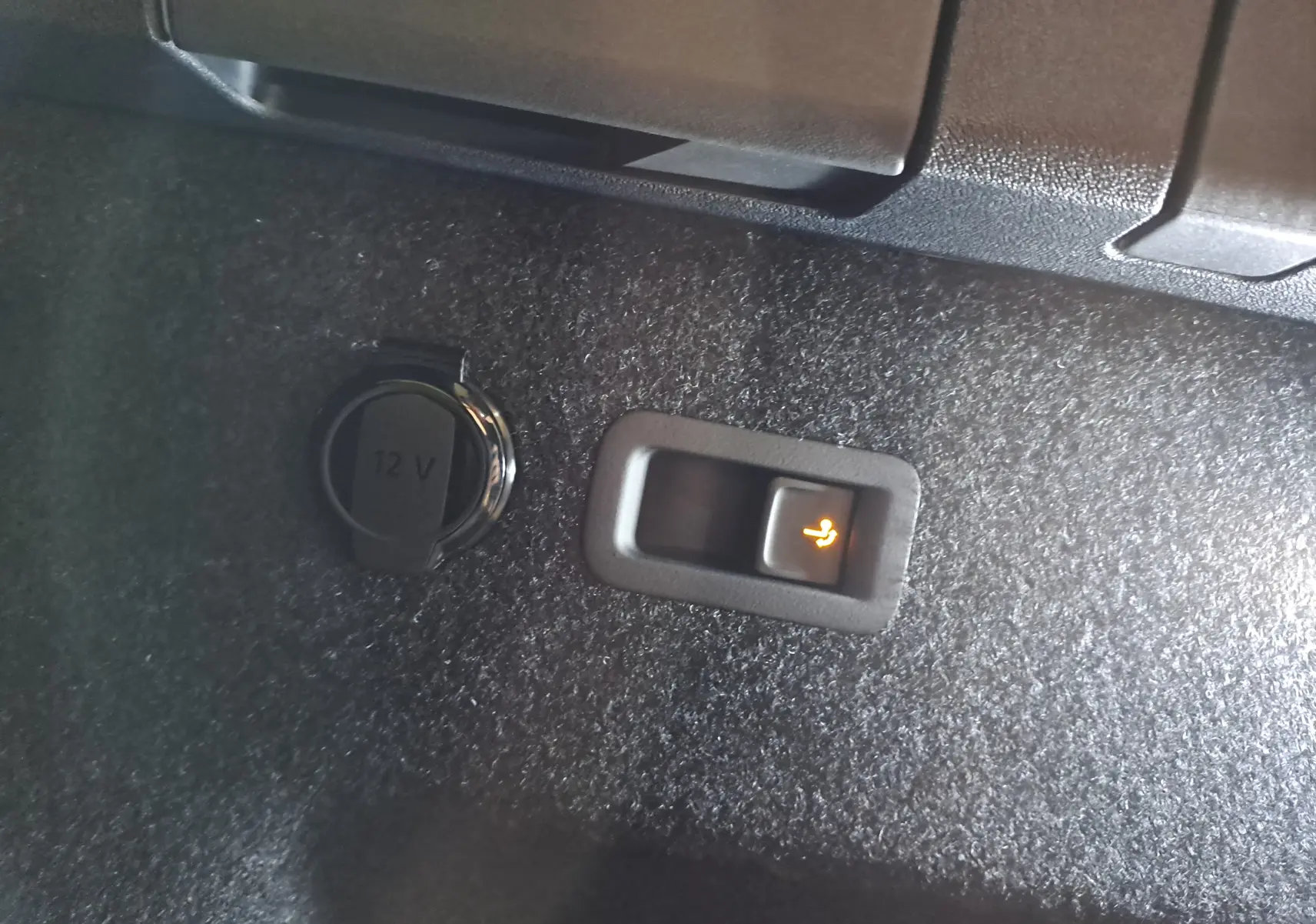 Détail intérieur du coffre du Skoda Kodiaq gris argent, bouton d'ouverture électrique du hayon et prise 12V visibles.