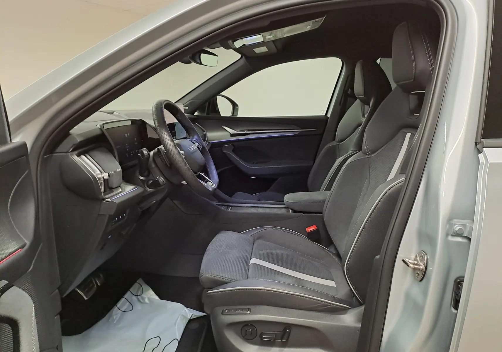 Vue intérieure côté conducteur du Skoda Kodiaq gris argent 2025, sièges sport noirs avec surpiqûres grises et tableau de bord moderne.
