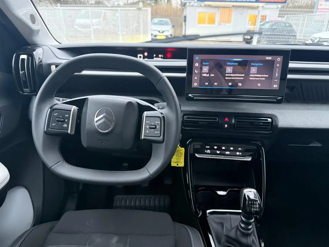 Vue intérieure avant du poste de conduite gris de la Citroën C3 2025 avec volant multifonction et écran tactile central.