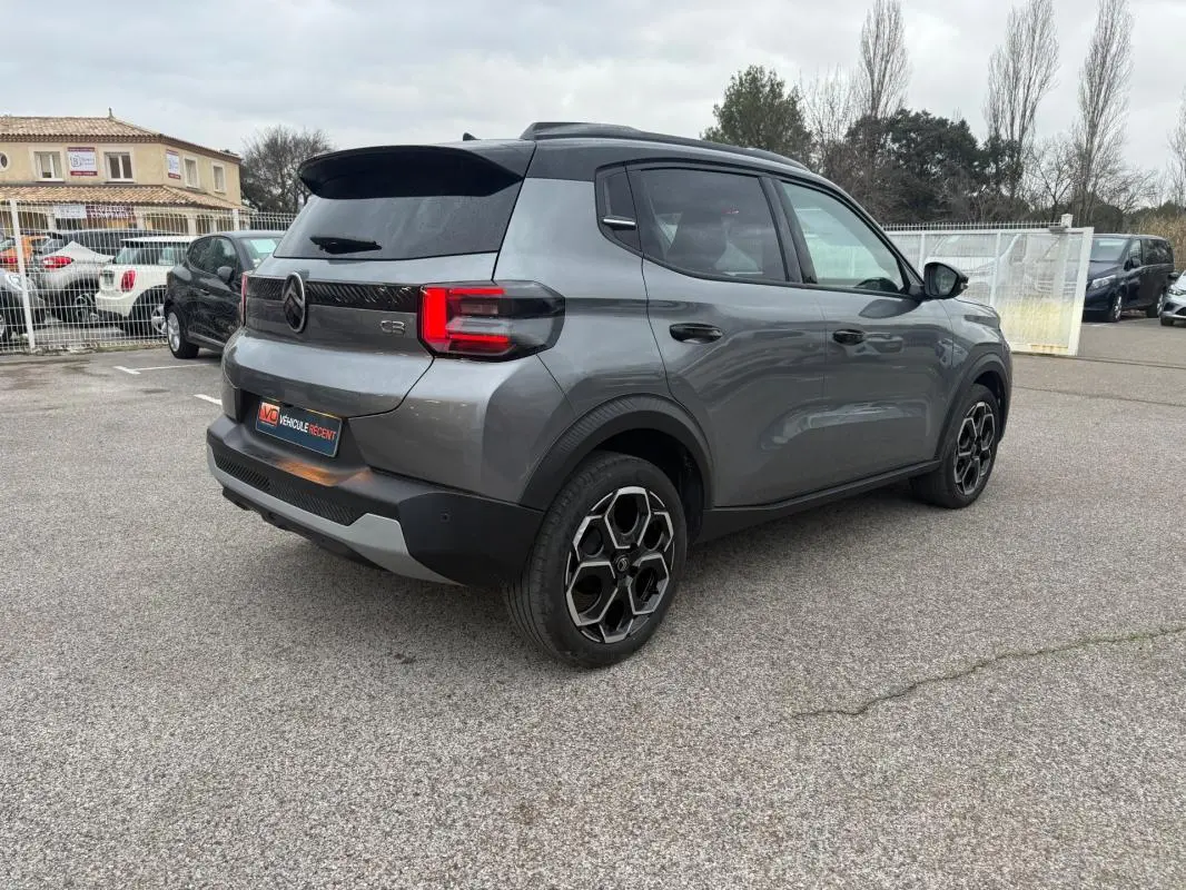 Vue 3/4 arrière droite d'une Citroën C3 gris 2025 avec jantes alliage 17 pouces et barres de toit visibles.