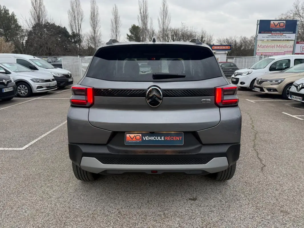Vue arrière d'une Citroën C3 gris 2025 avec feux LED allumés et barres de toit visibles sur un parking.