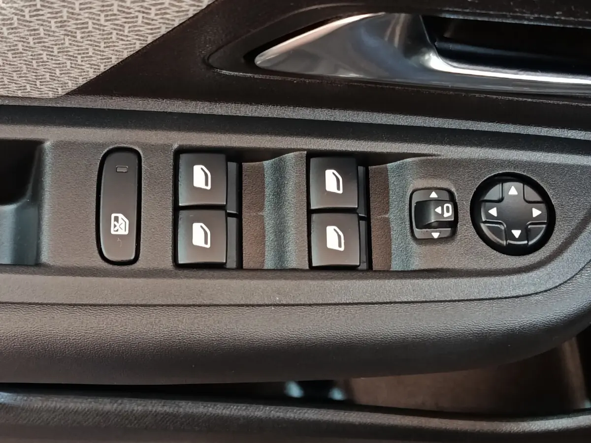 Gros plan sur les commandes de lève-vitres et réglages des rétroviseurs côté conducteur d'une Citroën C4 gris foncé.