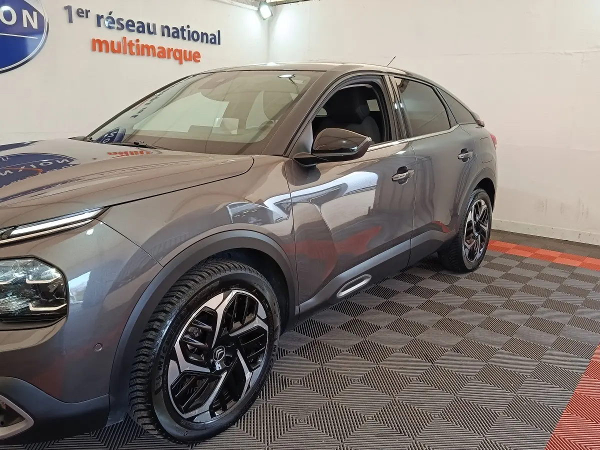 Vue 3/4 avant droit d'une Citroën C4 gris foncé avec jantes noires et détails chromés, stationnée en intérieur.