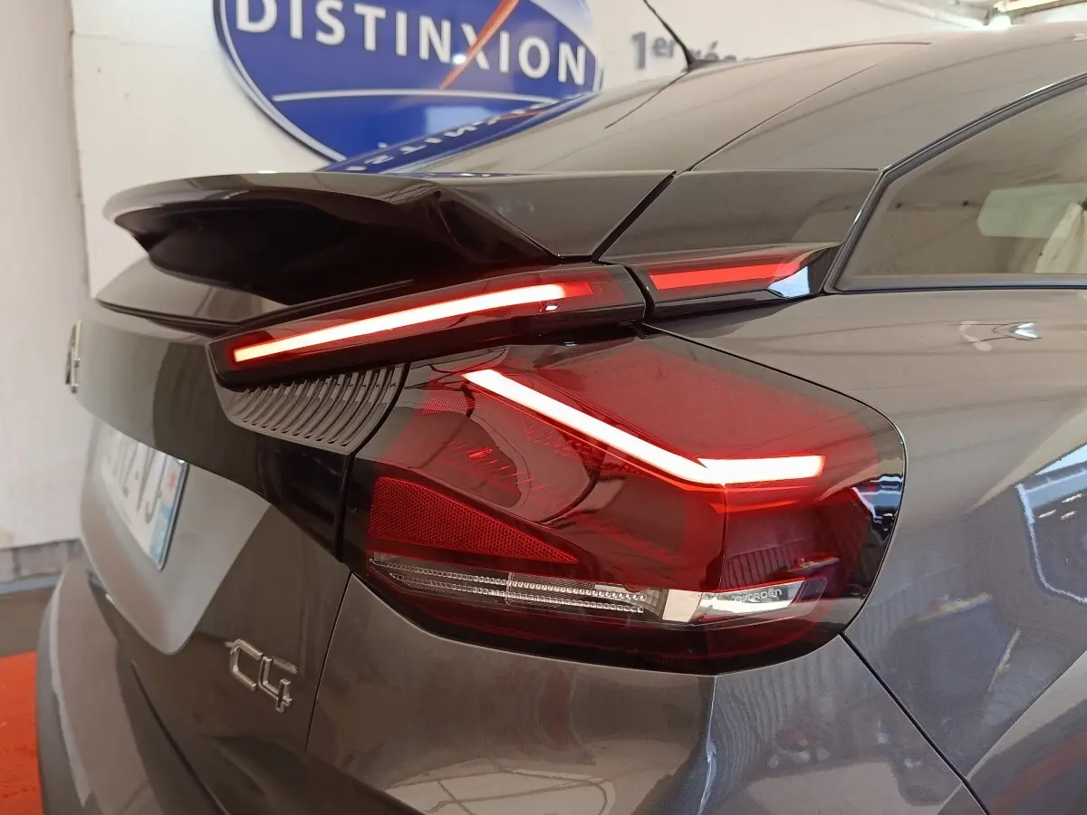 Feu arrière allumé en gros plan côté gauche d'une Citroën C4 gris foncé, avec aileron et logo visible.