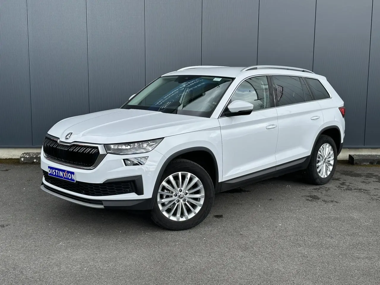 Vue 3/4 avant droit d'un Skoda Kodiaq blanc glacier avec jantes alliage 18 pouces sur fond urbain.