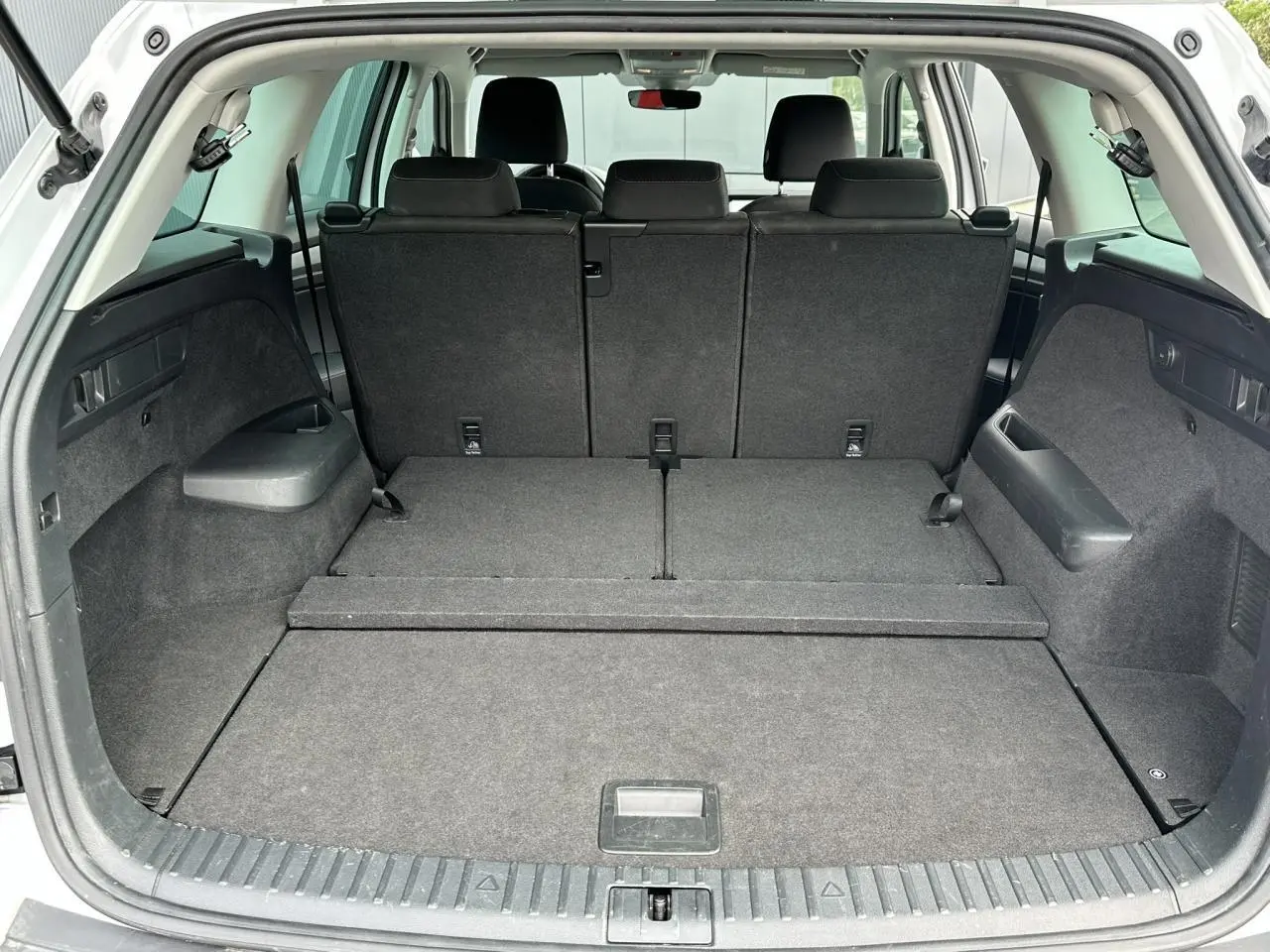 Coffre ouvert du Skoda Kodiaq blanc glacier 2024, montrant la banquette arrière rabattue et l'espace de chargement spacieux.